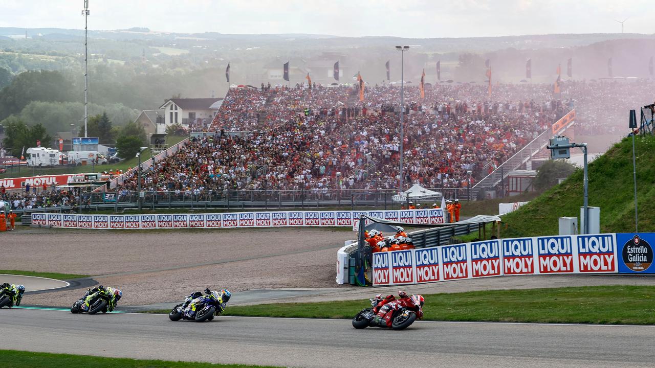 Renn-Motorräder auf der Strecke, im Hintergrund eine volle Tribüne