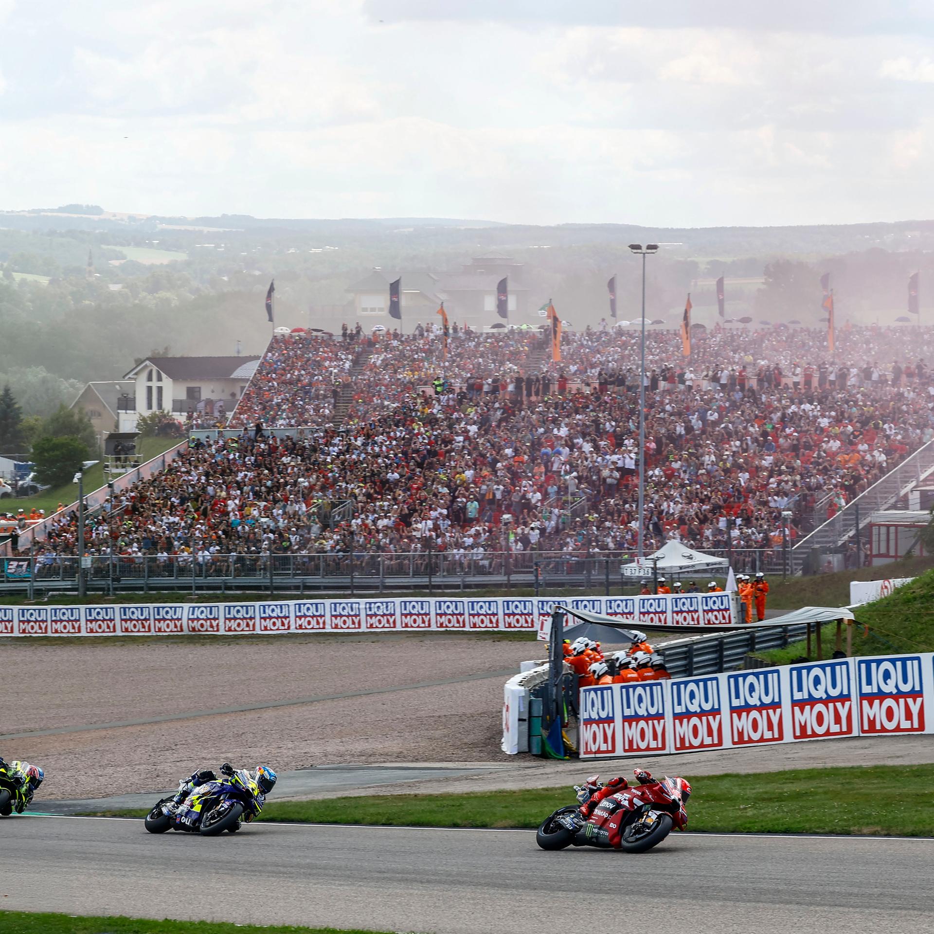 Renn-Motorräder auf der Strecke, im Hintergrund eine volle Tribüne
