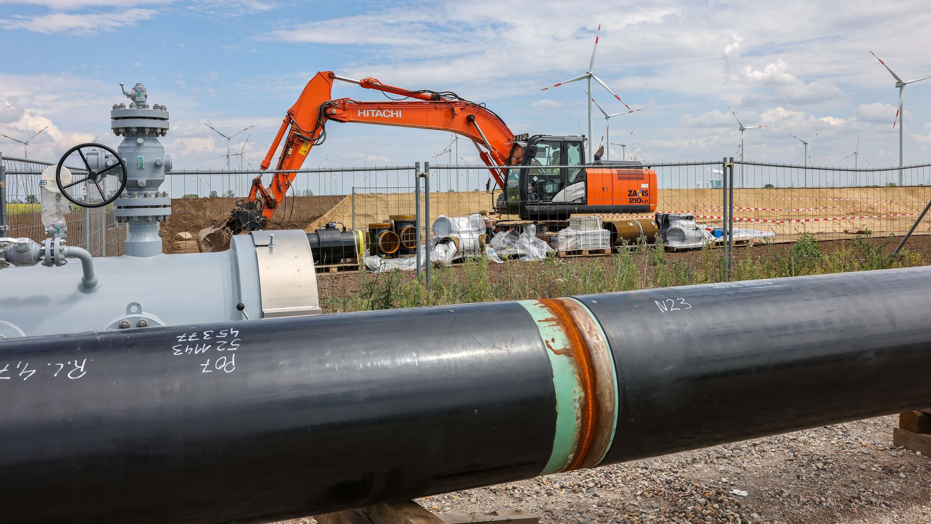 Die Rohre einer künftigen Wasserstoffleitung liegen vor der Kulisse eines Windparks. 