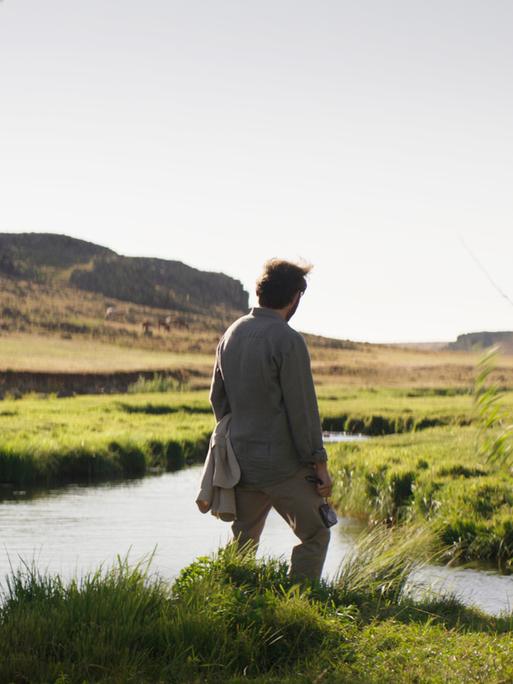 Filmszene aus "Auf trockenen Gräsern". Ein Mann steht alleine an einem Flussufer.