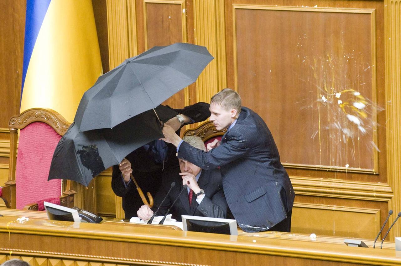 Männer in Anzügen schützen sich mit Regenschirmen vor Eierwürfen 2010 im ukrainischen Parlament.