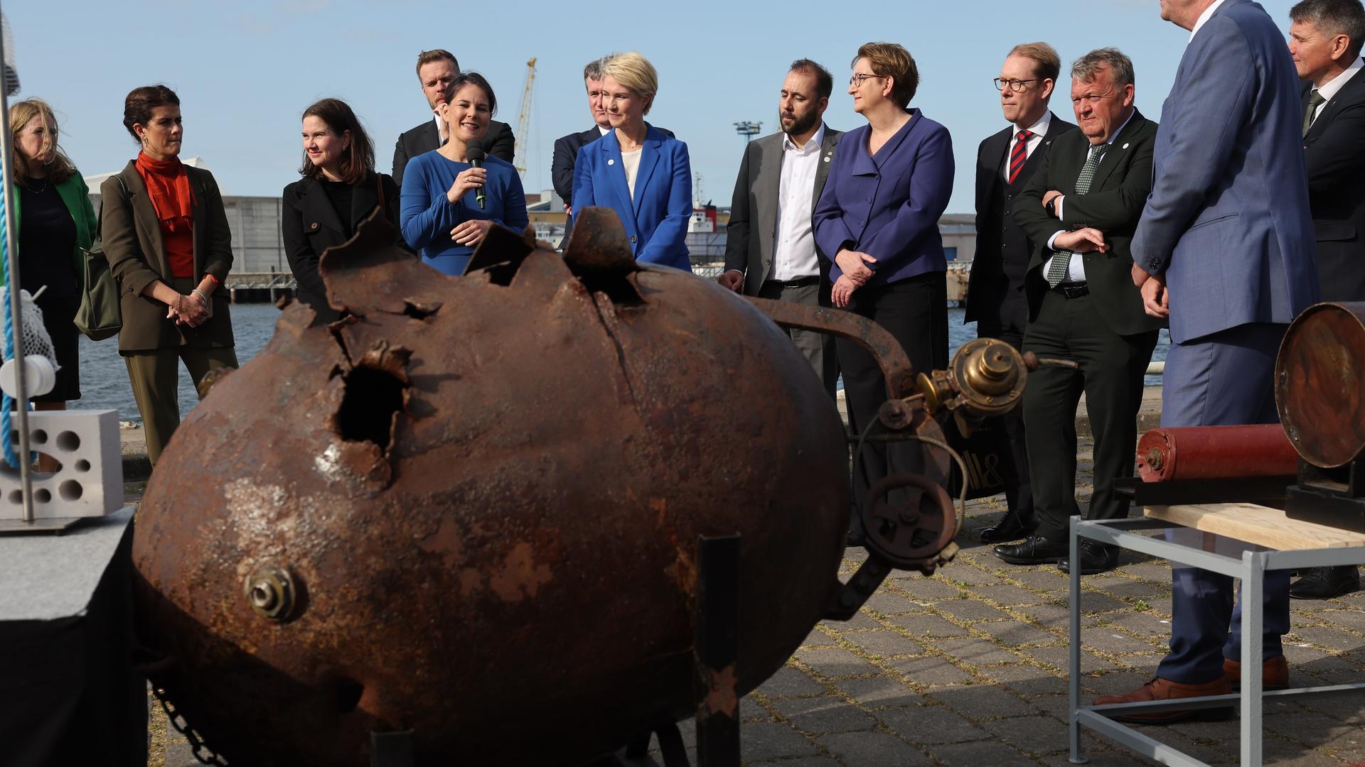 Außenministerin Baerbock erklärt am Mikrofon im Hafen von Wismar die Funktionsweise einer Wassermine aus dem 1. Weltkrieg.