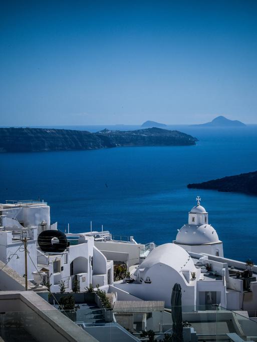 Weiße Häuser auf der griechischen Insel Santorini, im Hintergrund das Mittelmeer und weitere Inseln.