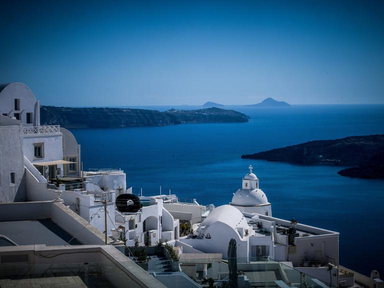 Weiße Häuser auf der griechischen Insel Santorini, im Hintergrund das Mittelmeer und weitere Inseln.