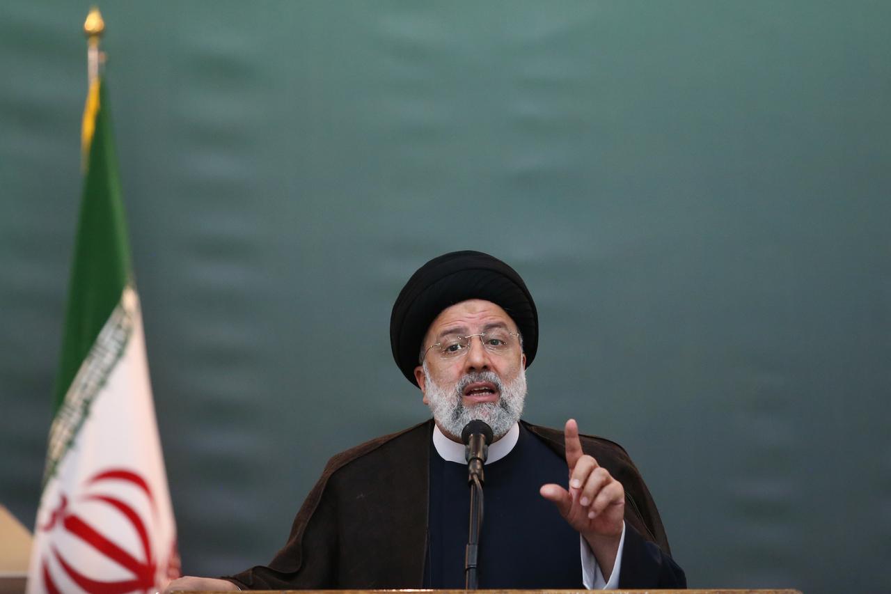 Der iranische Präsident Ebrahim Raisi vor grünem Hintergrund, vor ihm ein Mikrofon. Er hält eine Rede mit erhobenem Zeigefinger.