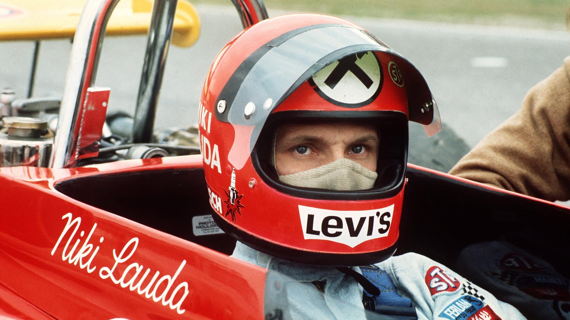 Der österreichische Rennfaher Niki Lauda in seinem roten Rennwagen, aufgenommen während des Clark-Gedächtnisrennens im April 1972. Der österreichische Rennfaher Niki Lauda sitzt in einem roten Rennwagen mit Niki Lauda-Schriftzug. Er trägt einen Helm und eine Gesichtsmaske.