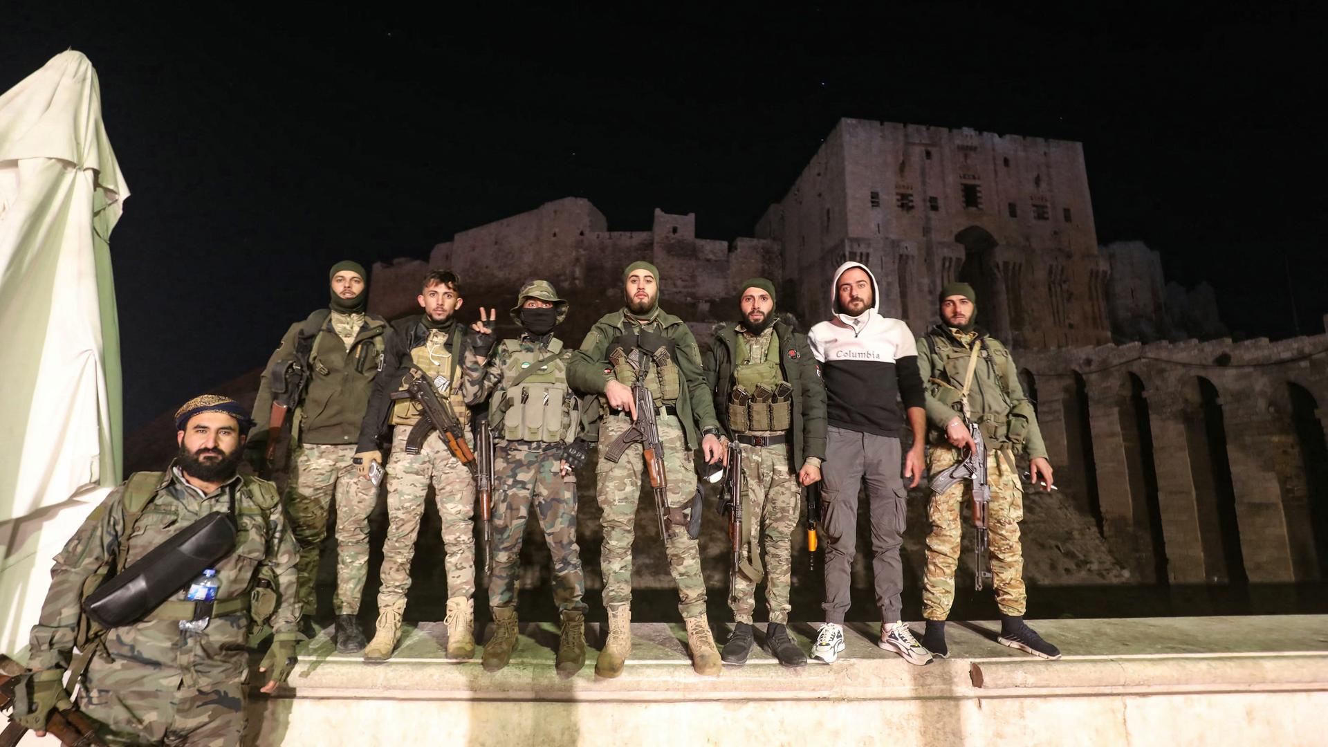 Männer in Uniformen stehen in einer Reihe und posieren für ein Foto. Es ist Nacht. Die Männer stehen vor einer Zitadelle in der Stadt Aleppo im Land Syrien. 