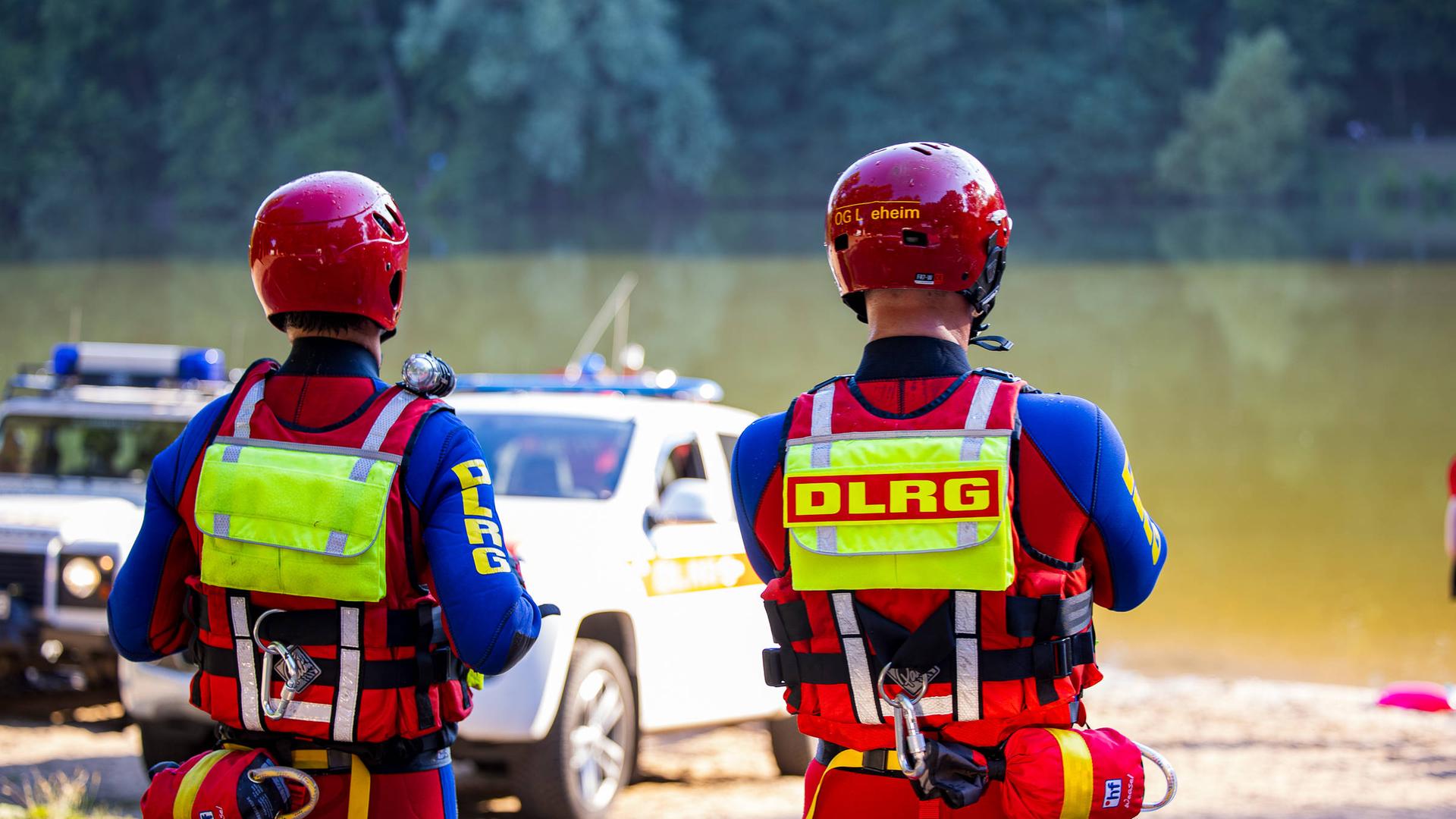 2 Mitarbeiter von der DLRG stehen am Ufer von einem See. Sie beobachten Rettungs-Arbeiten. 