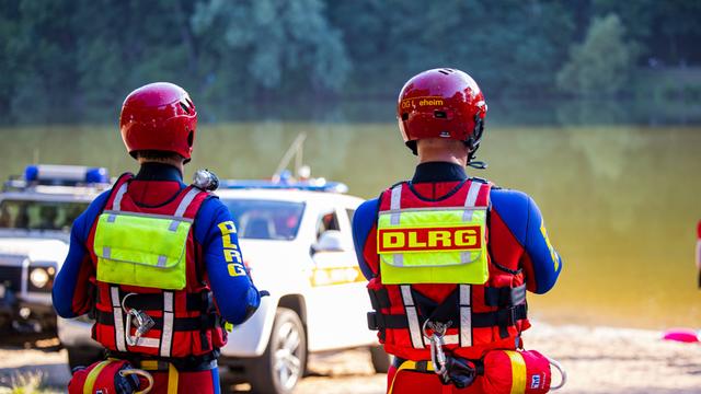 2 Mitarbeiter von der DLRG stehen am Ufer von einem See. Sie beobachten Rettungs-Arbeiten. 