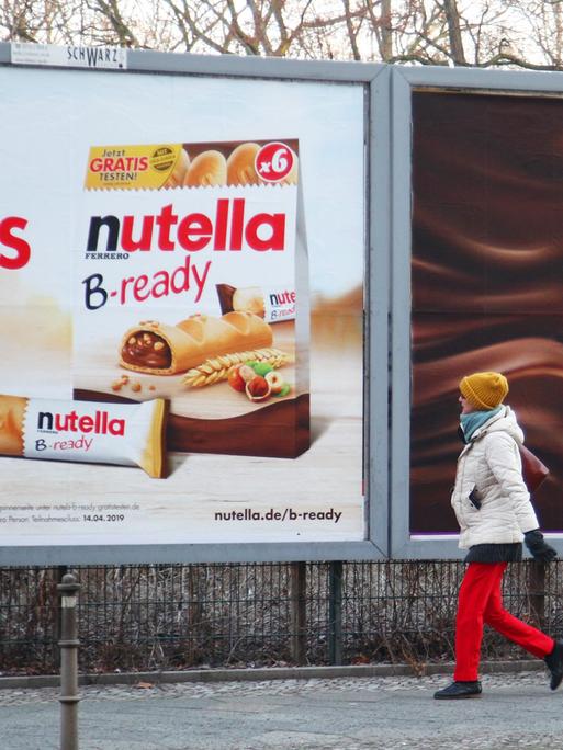 Eine Fußgängerin geht bei Kälte an einem Großplakat mit Webung für Duplo und Nutella B-ready von Ferrero vorbei.