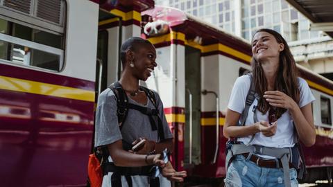 Zwei junge Frauen lachen auf einem Bahnsteigt sich an. Man sieht, dass sie sie gut verstehen.