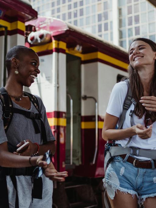 Zwei junge Frauen lachen auf einem Bahnsteigt sich an. Man sieht, dass sie sie gut verstehen. Zwei junge Frauen lachen auf einem Bahnsteigt sich an. Man sieht, dass sie sie gut verstehen.