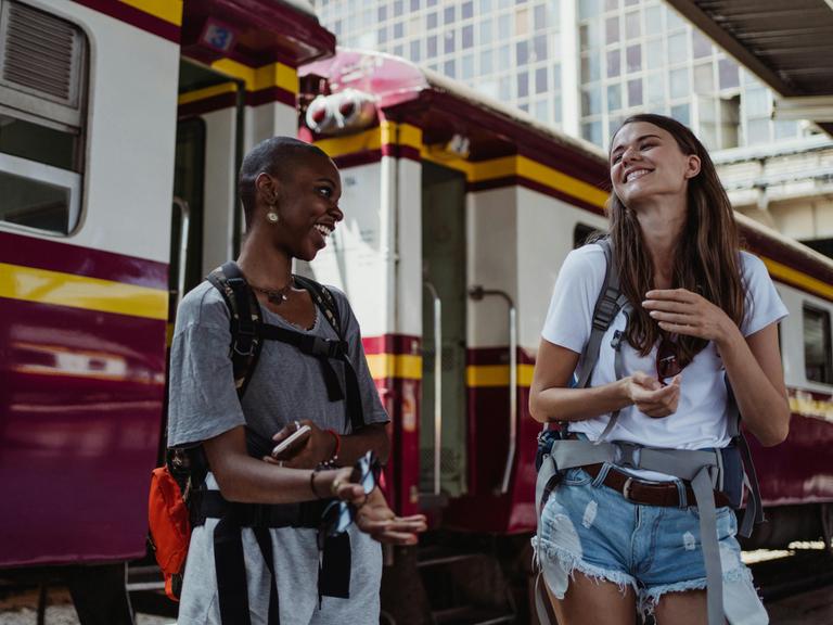 Zwei junge Frauen lachen auf einem Bahnsteigt sich an. Man sieht, dass sie sie gut verstehen. Zwei junge Frauen lachen auf einem Bahnsteigt sich an. Man sieht, dass sie sie gut verstehen.