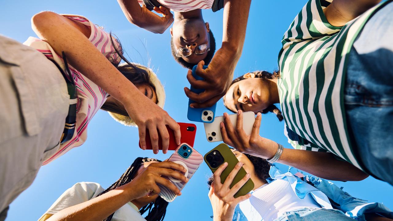 Untersicht auf fünf Teenager, die alle ein Smartphone in der Hand halten und drauf schauen.