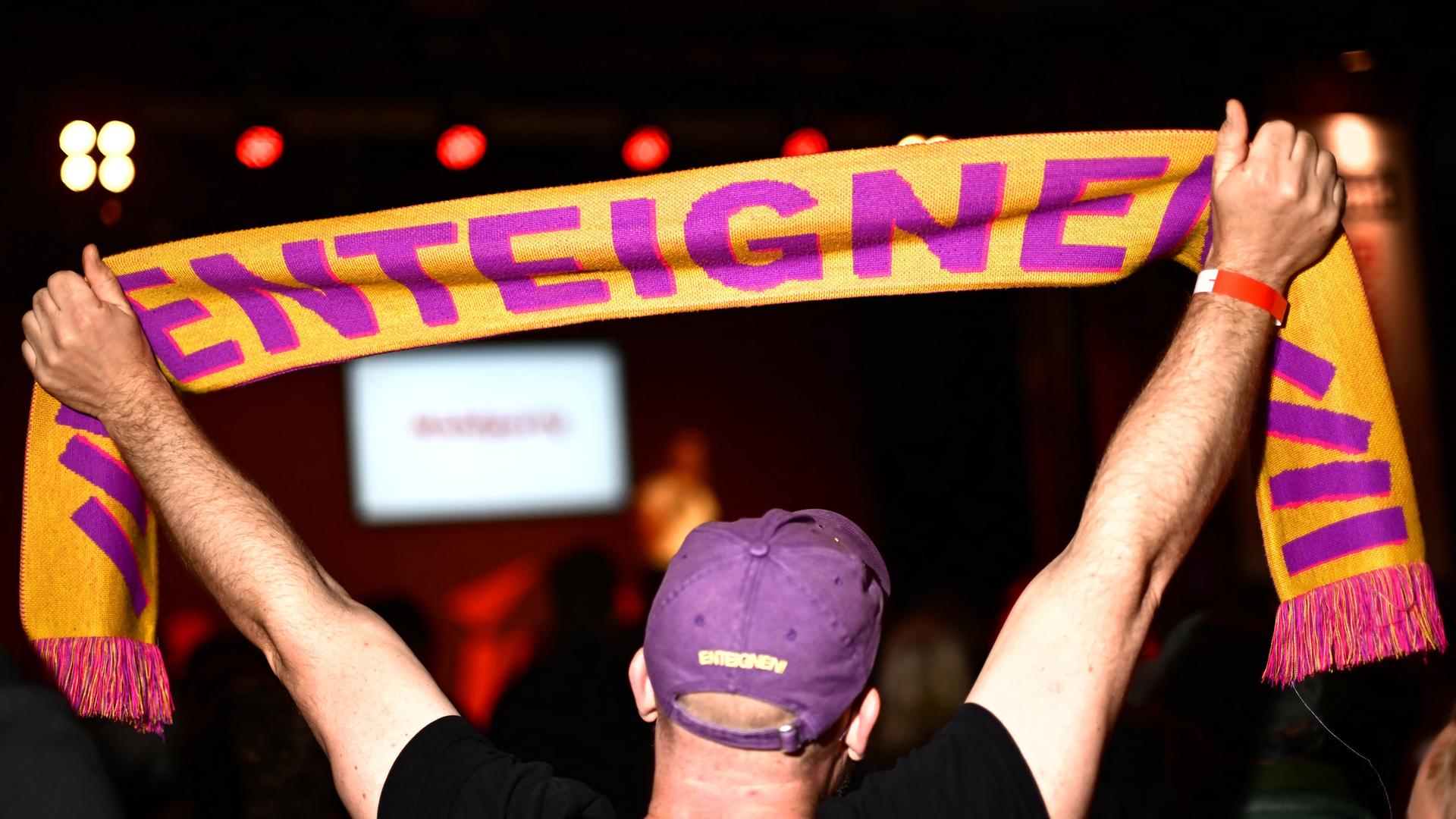 Ein Mann hält während der Wahlparty der Berliner Linken im Festsaal Kreuzberg einen Schal mit der Aufschrift "ENTEIGNEN" in die Höhe. Ein Mann hält während der Wahlparty der Berliner Linken im Festsaal Kreuzberg einen Schal mit der Aufschrift "ENTEIGNEN" in die Höhe.