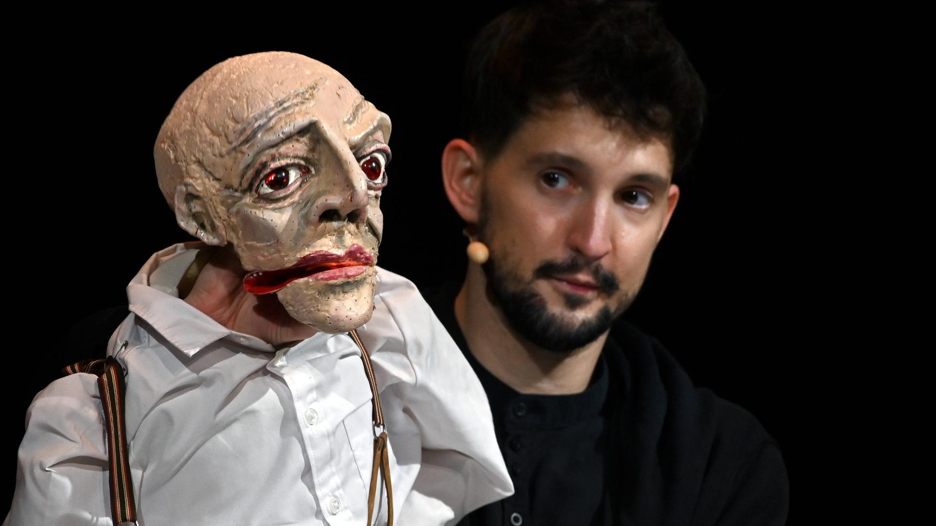 Der Puppenspieler Nikolaus Habjan mit einer Puppe bei einem Auftritt vor schwarzem Hintergrund.