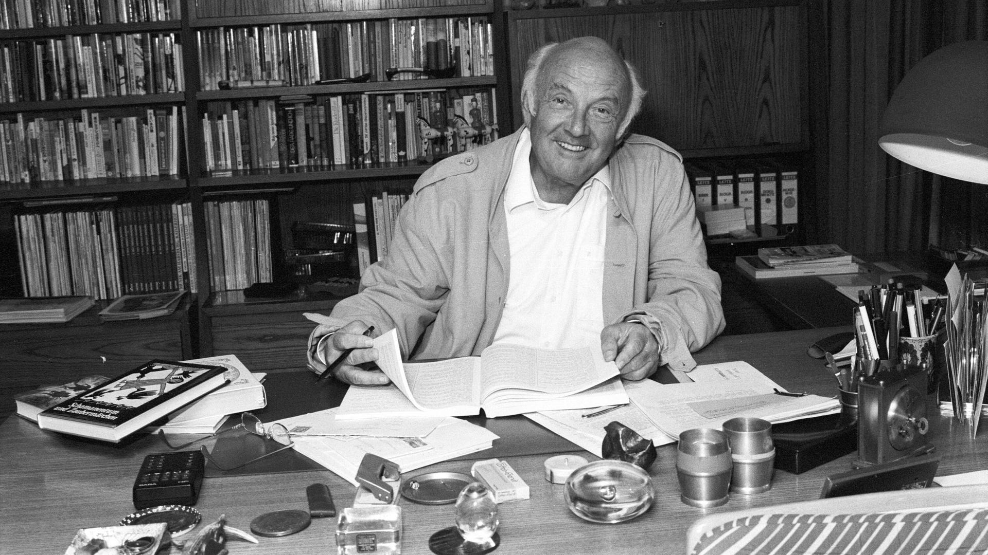 Schwarzweißfoto von Otfried Preußler, der an seinem Schreibtisch sitzt und in Unterlagen blättert