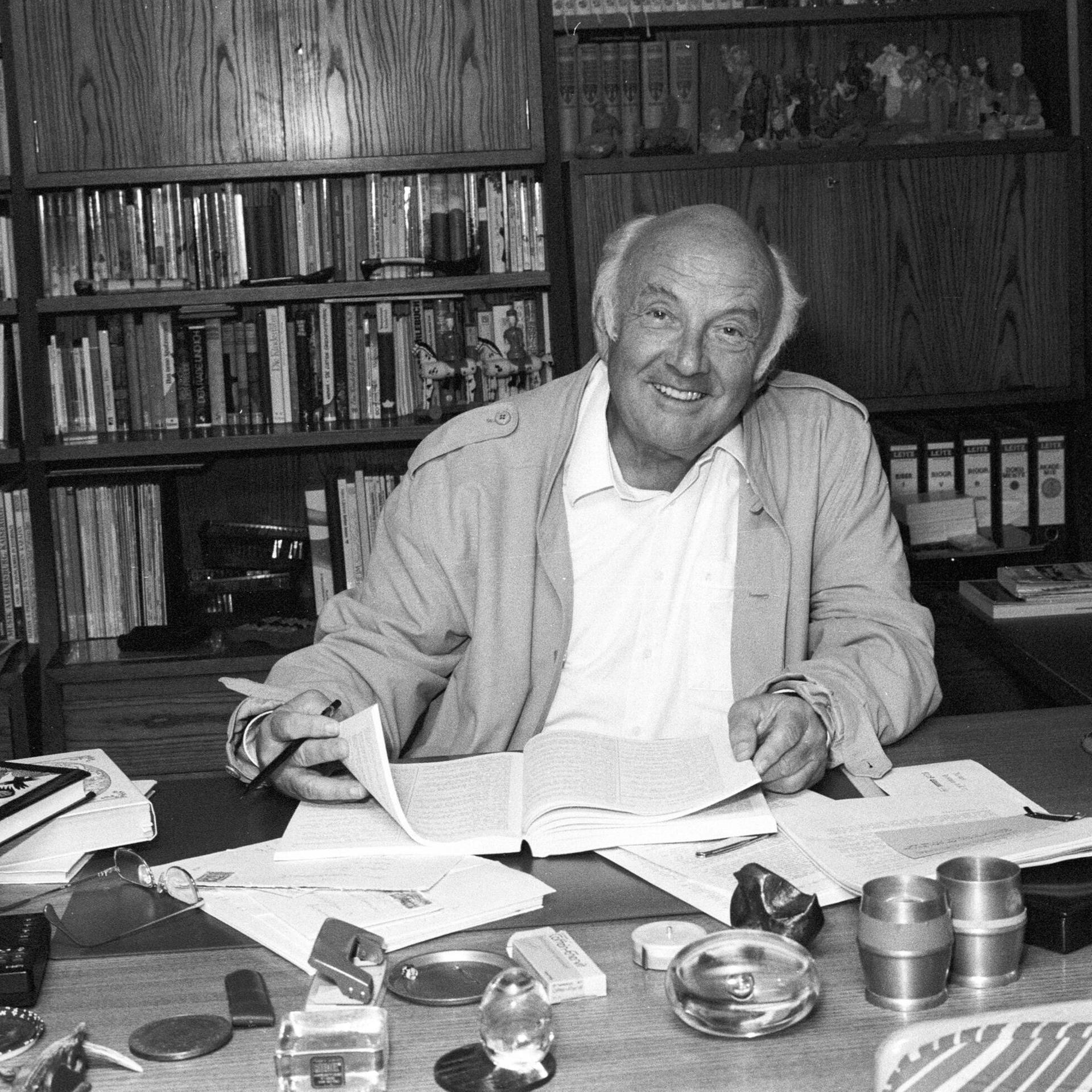 Schwarzweißfoto von Otfried Preußler, der an seinem Schreibtisch sitzt und in Unterlagen blättert