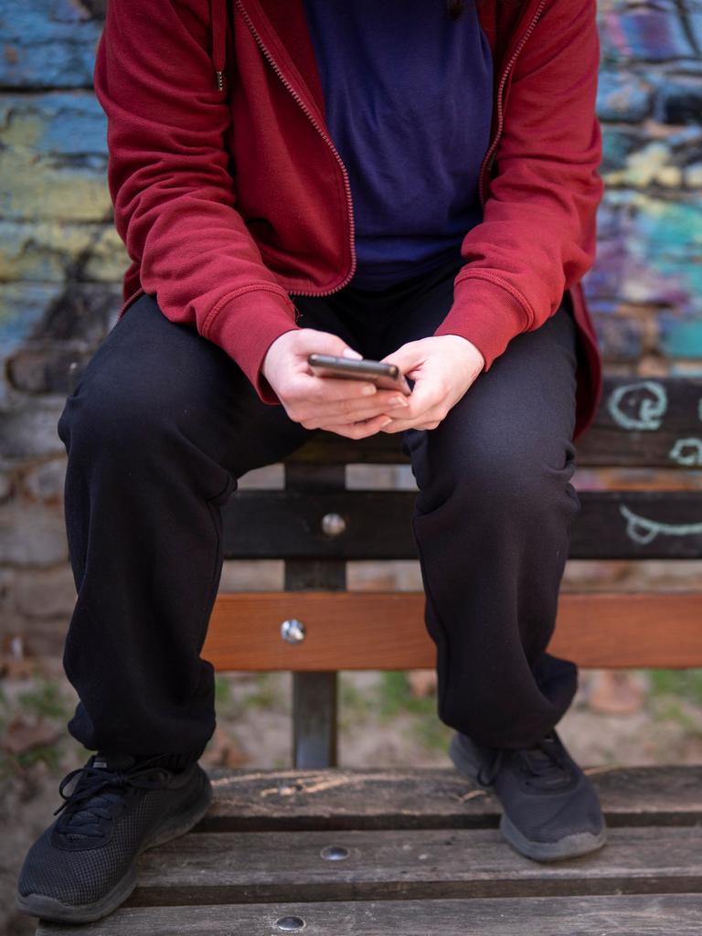 Jugendliche sitzen vor einer Graffiti-Wand auf einer Bank und schauen auf ihre Handys. Jugendliche sitzen vor einer Graffiti-Wand auf einer Bank und schauen auf ihre Handys.