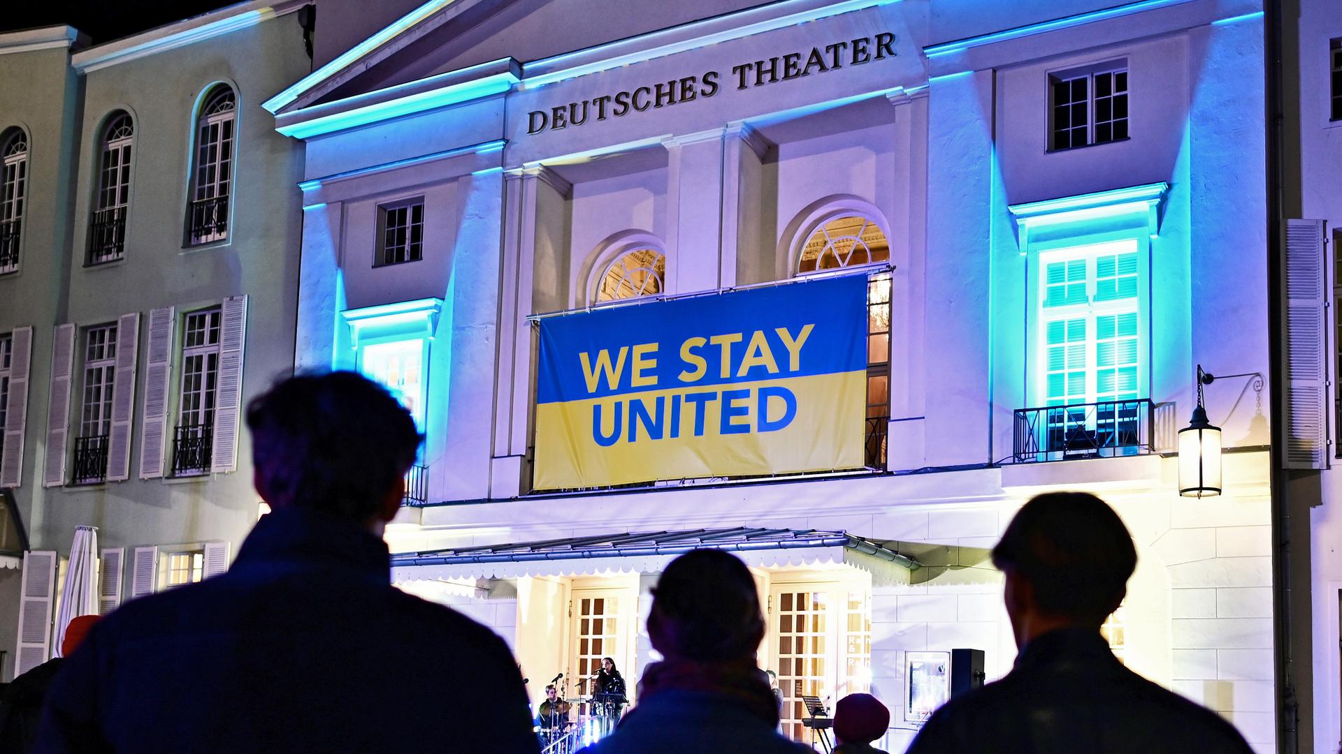 Fassade des Deutsches Theater in Berlin, über dem Eingang hängt ein blau-gelbes Banner mit der Aufschrift "we stay united".