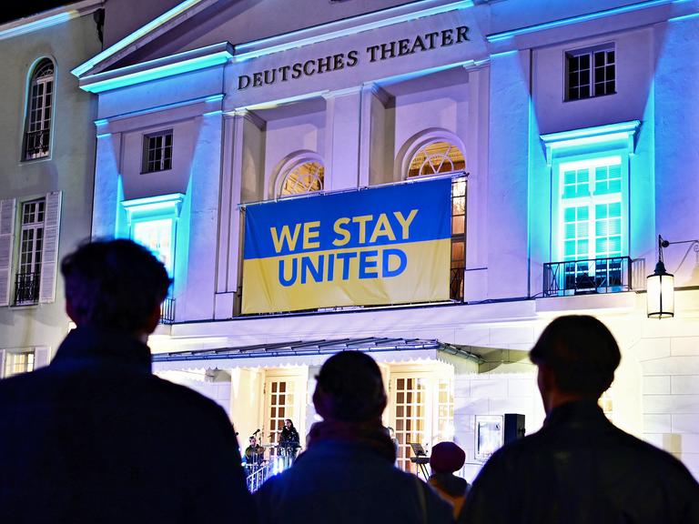 Fassade des Deutsches Theater in Berlin, über dem Eingang hängt ein blau-gelbes Banner mit der Aufschrift "we stay united".