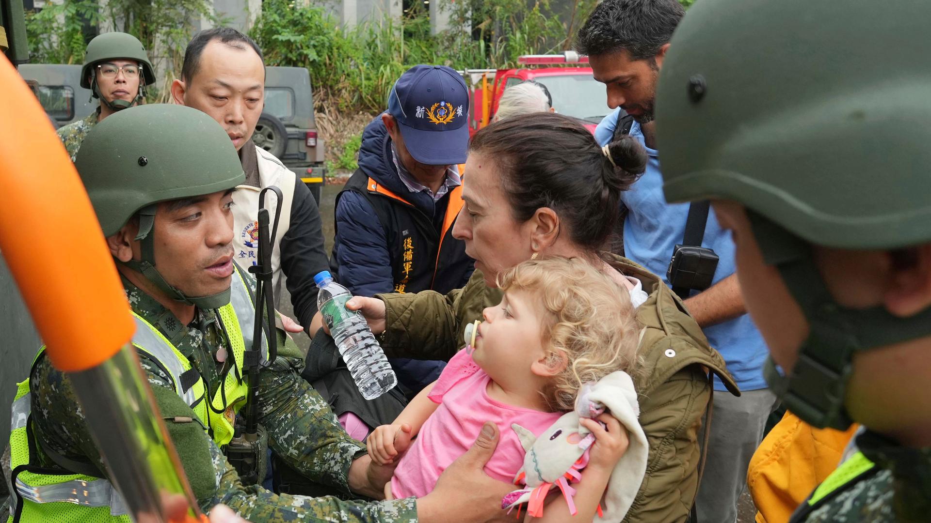 Retter in Taiwan befreien eine Mutter und ihr Kind. Die Retter tragen Uniformen. Das kleine Kind ist im Arm der Mutter. 
