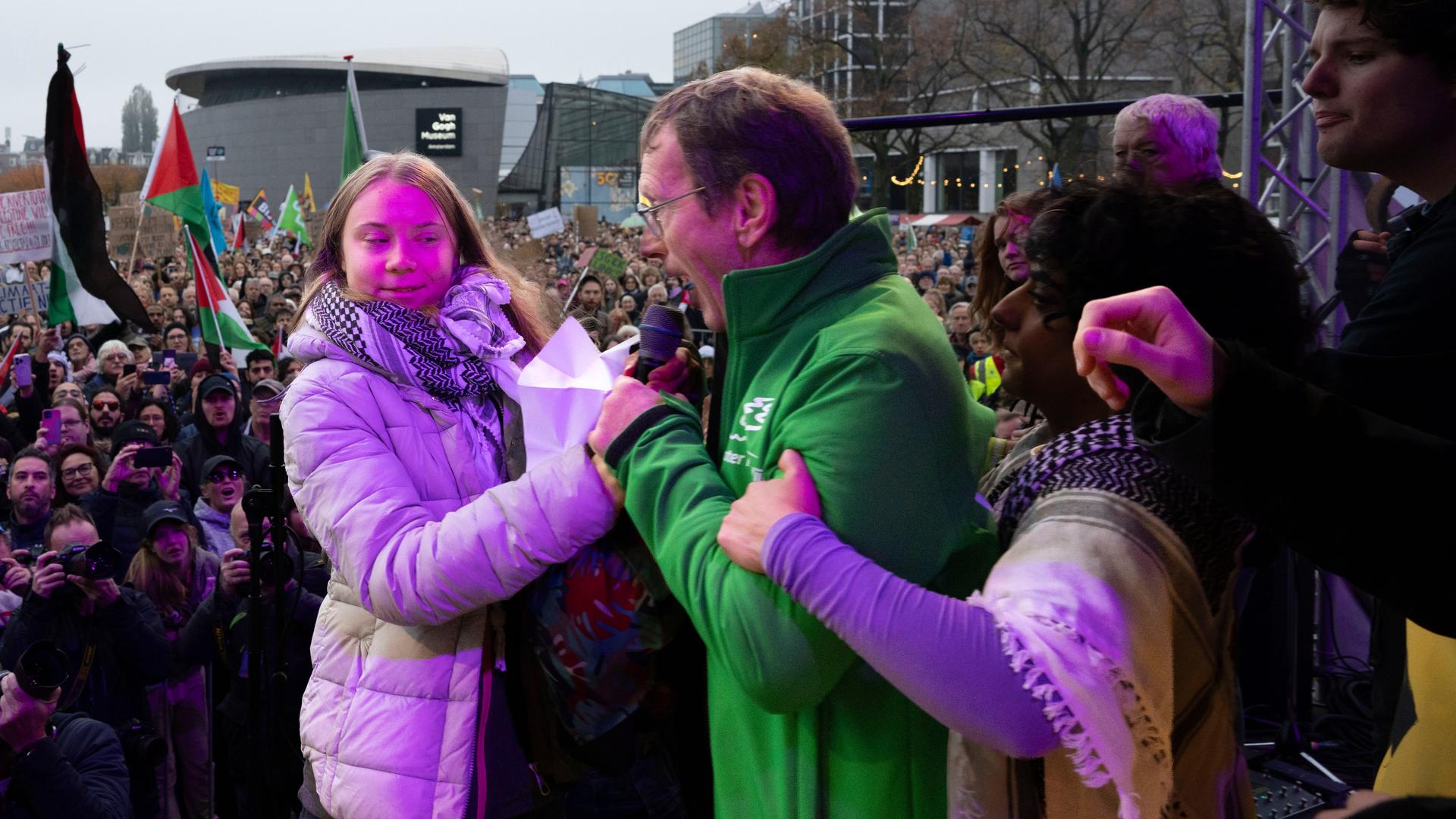 The picture shows climate activist Greta Thunber on a stage in Amsterdam, to her left a man from the audience in a green jacket who has taken the microphone away from her.