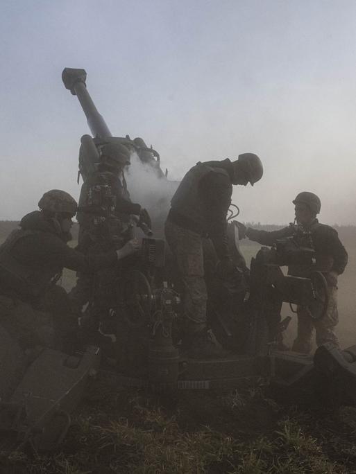 Eine Artillerieeinheit in der Region Cherson im November 2022. Drei Soldaten bedienen das Geschütz. Es wird von Rauchschwaden umgeben.