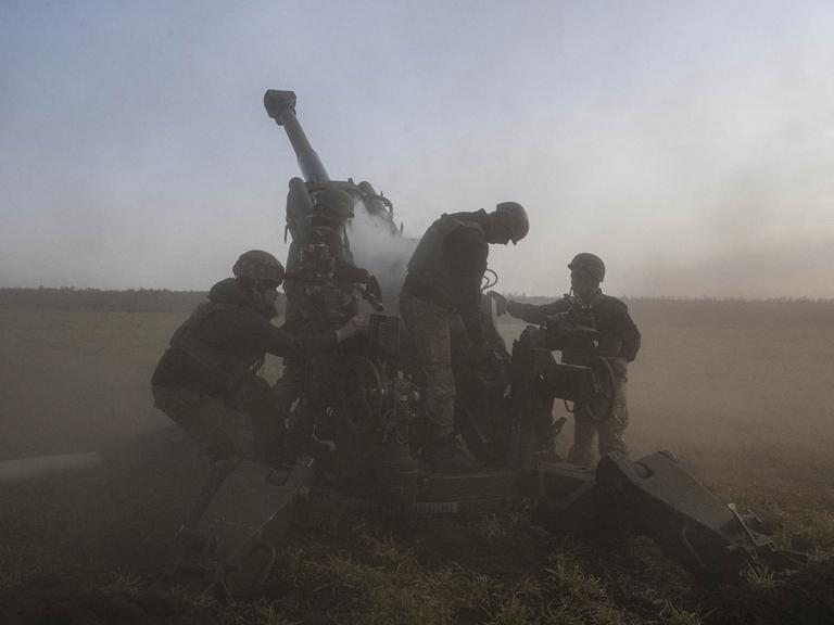 Eine Artillerieeinheit in der Region Cherson im November 2022. Drei Soldaten bedienen das Geschütz. Es wird von Rauchschwaden umgeben.