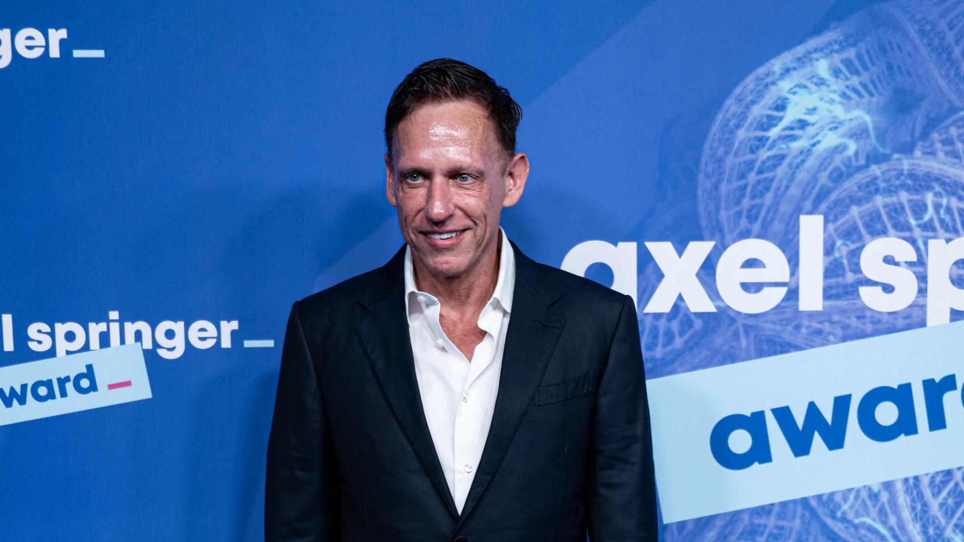 Peter Thiel steht vor einer Wand und lächelt. Auf der Wand ist der Schriftzug "Axel Springer" zu sehen. Peter Thiel steht vor einer Wand und lächelt. Auf der Wand ist der Schriftzug "Axel Springer" zu sehen.