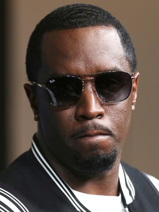 Sean „Diddy“ Combs kommt in dunkler Sonnenbrille und einer schwarz-weissen Collegejacke zur LA-Premiere von "The Four: Battle For Stardom" im CBS Radford Studio Center 2018, in Los Angeles. Seine Miene ist ernst, die Lippen aufeinander gespresst.