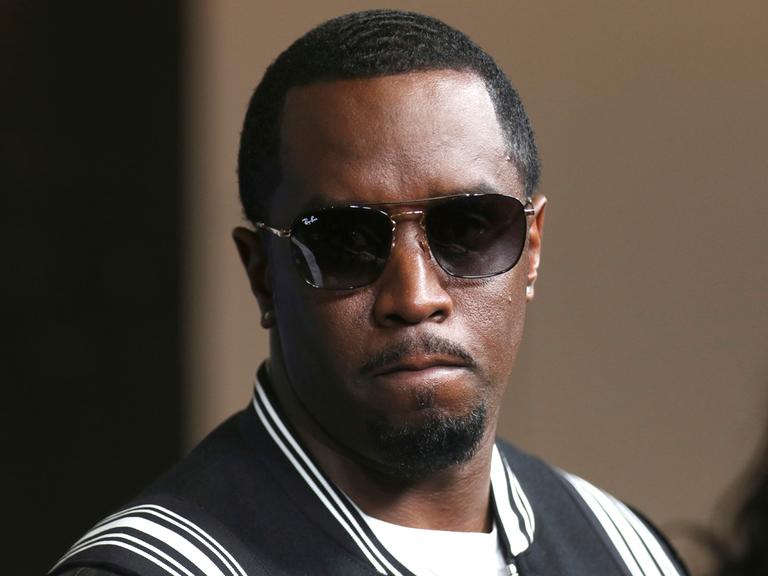 Sean „Diddy“ Combs kommt in dunkler Sonnenbrille und einer schwarz-weissen Collegejacke zur LA-Premiere von "The Four: Battle For Stardom" im CBS Radford Studio Center 2018, in Los Angeles. Seine Miene ist ernst, die Lippen aufeinander gespresst.