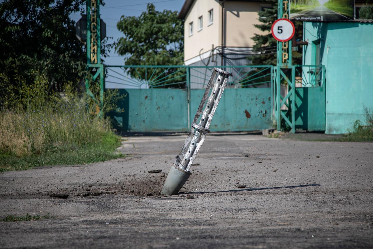 Die Rakete steckt fast senkrecht in einem Feldweg. Dahinter ein Gebäude mit blauem Schiebetor.  