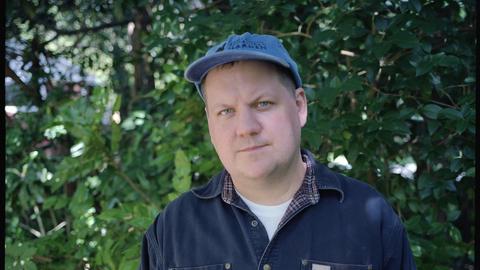 Der US-amerikanische Folkmusiker Jake Xerxes Fussell trägt Jeans-Hemd und Trucker-Mütze