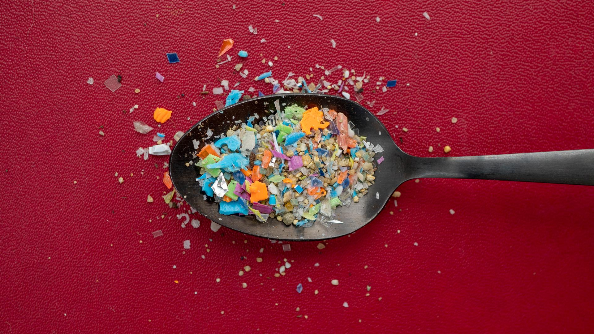 Ein Häufchen Mikroplastik auf einem Löffel vor dunkelrotem Hintergrund.