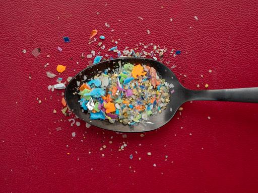 Ein Häufchen Mikroplastik auf einem Löffel vor dunkelrotem Hintergrund.