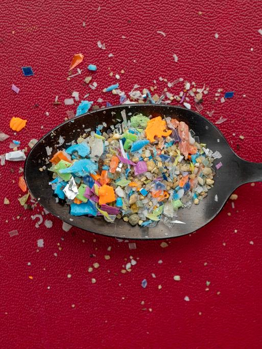 Ein Häufchen Mikroplastik auf einem Löffel vor dunkelrotem Hintergrund.