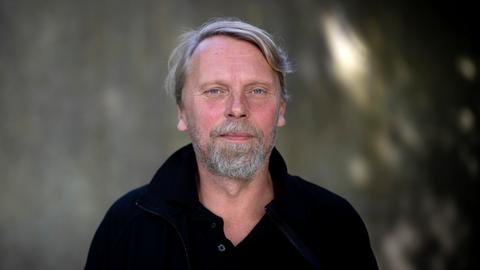Der Schriftsteller und Journalist Jens Balzer im Portrait mit grauem Bart vor dunklem Hintergrund. Der Schriftsteller und Journalist Jens Balzer im Portrait mit grauem Bart vor dunklem Hintergrund.