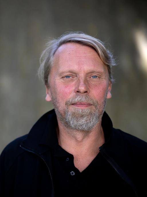Der Schriftsteller und Journalist Jens Balzer im Portrait mit grauem Bart vor dunklem Hintergrund. 