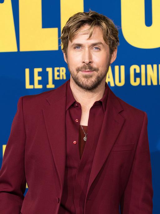 Das Bild zeigt Ryan Gosling in einem rotwein-farbenen Anzug bei einer Werbetour für einen Film.