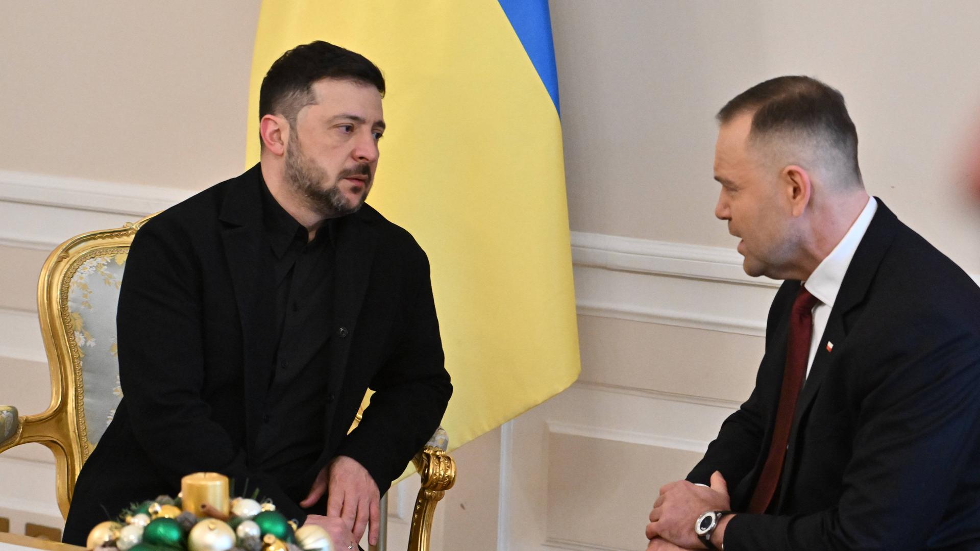 Wolodymyr Selenskyj und Karol Nawrocki sitzen während eines Gespräch in goldenen Stühlen. Im Hintergrund: eine Ukraine-Flagge.