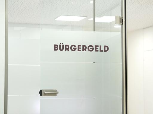 Das Wort "Bürgergeld" steht auf einer geöffneten Glastür 