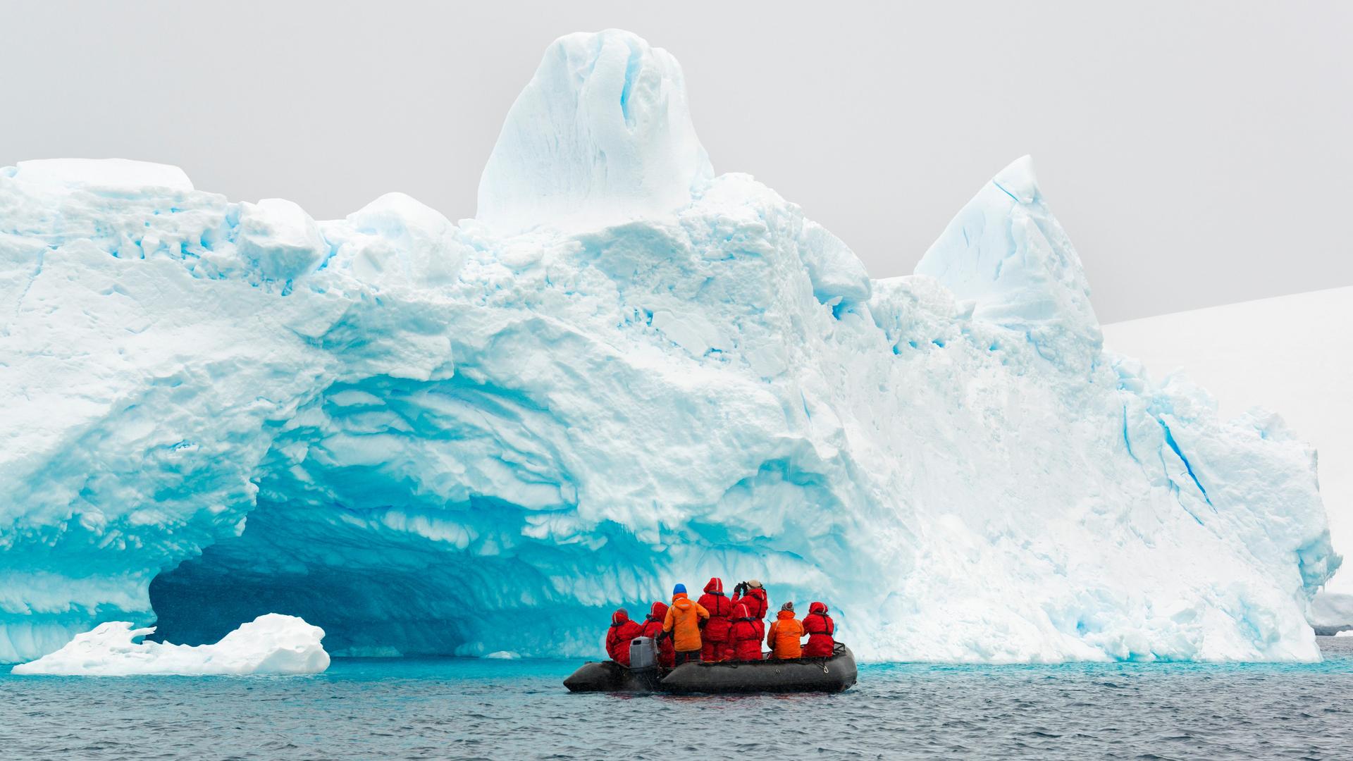 In der Antarktis fahren einige Forschende auf einem Gummiboot am Rand eines Eisbergs entlang.