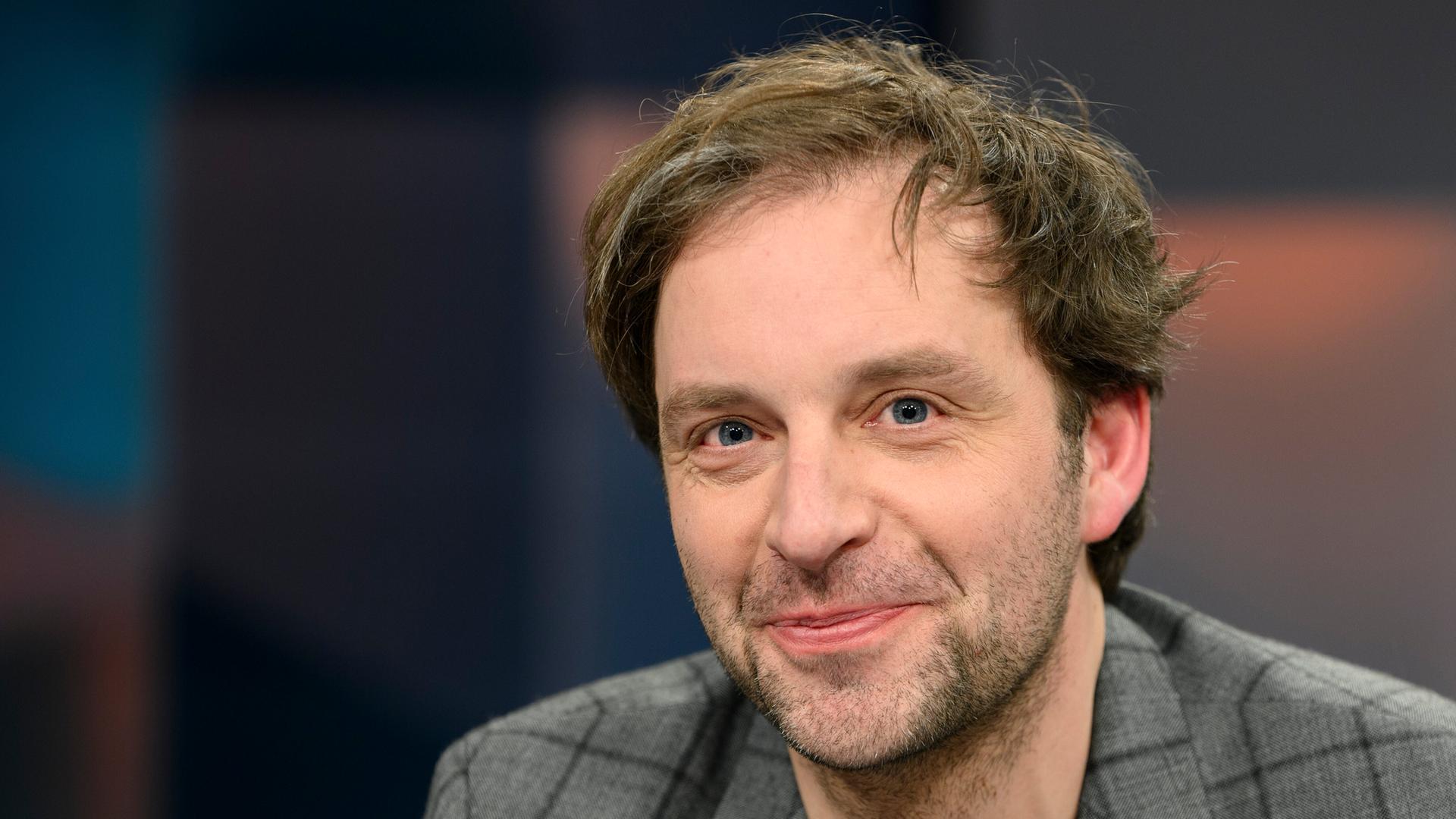 Nils Kumkar blickt verschmitzt lächelnd in die Kamera. 