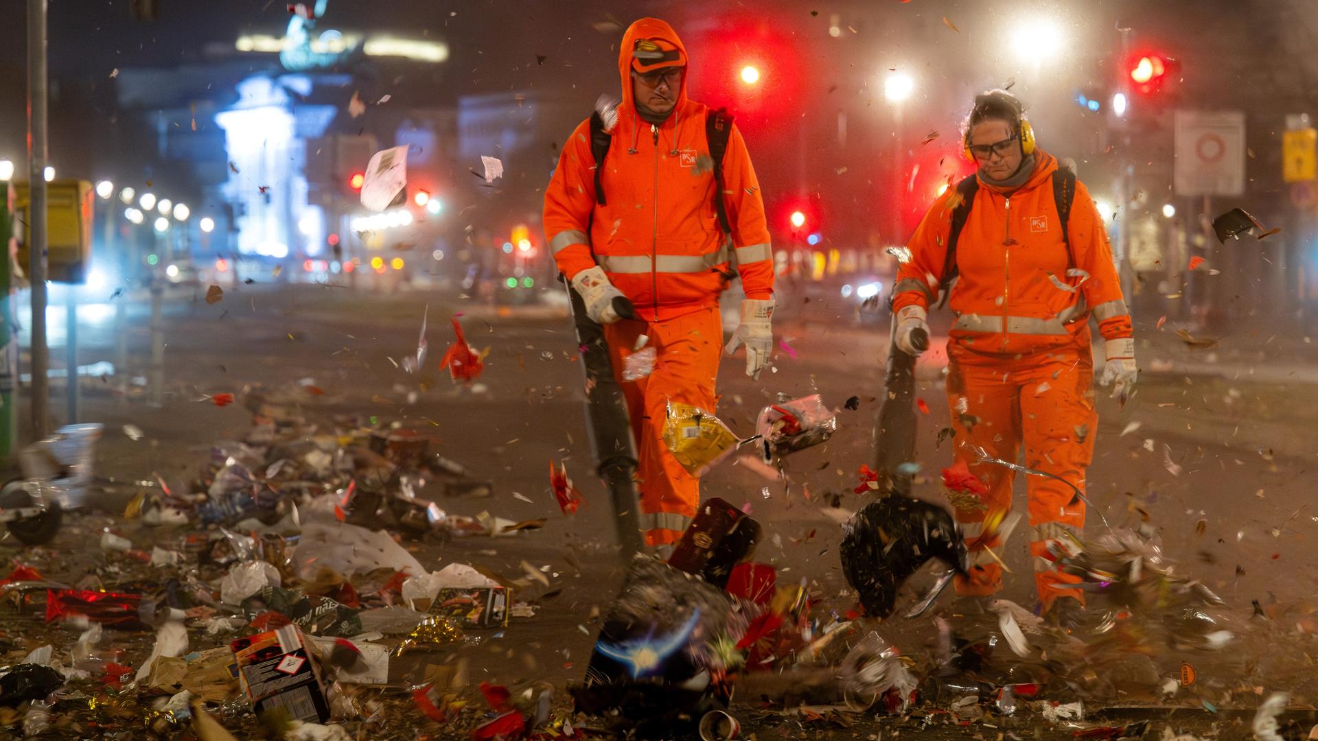 Mitarbeiter der Berliner Stadtreinigung (BSR) blasen mit Laubbläsern den Müll der Silvesternacht auf die Straße, wo er später von einer Kehrmaschine beseitigt wird. Für die Neujahrsreinigung sind rund 500 Mitarbeitende und 180 Fahrzeuge im Einsatz.