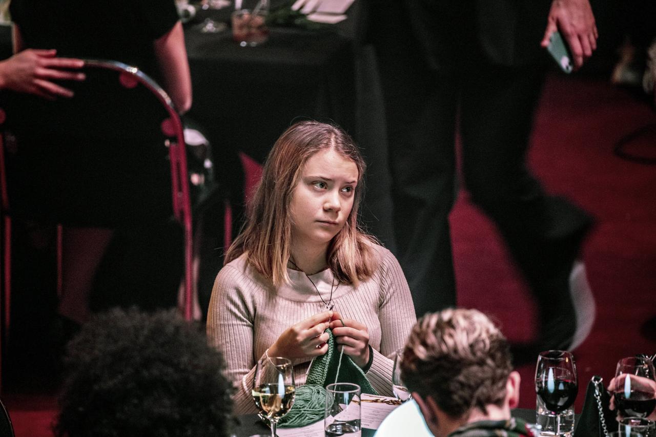 Greta Thunberg sitzt bei einer Veranstaltung häkelnd im Publikum.