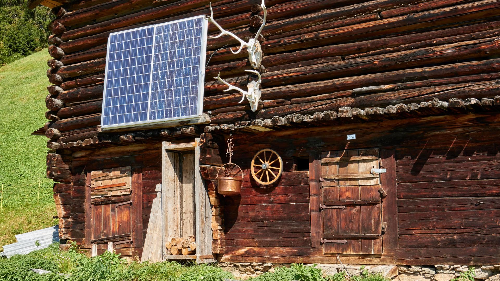 Teilansicht eines alten Holzstalls, bestückt mit Solarzellen und Hirschgeweihen. Surselva, Graubünden, Schweiz