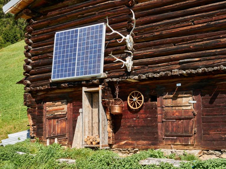 Teilansicht eines alten Holzstalls, bestückt mit Solarzellen und Hirschgeweihen. Surselva, Graubünden, Schweiz