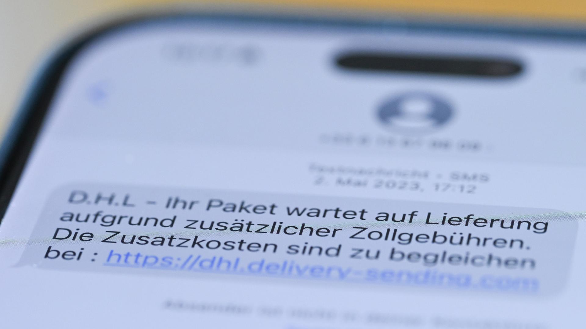 Nahaufnahme des Textes auf dem Handydisplay, der lautet: "DHL - ihr Paket wartet auf Lieferung aufgrund zusätzlicher Zollgebühren. Die Zusatzkosten sind zu begleichen." Danach folgt der Link. 