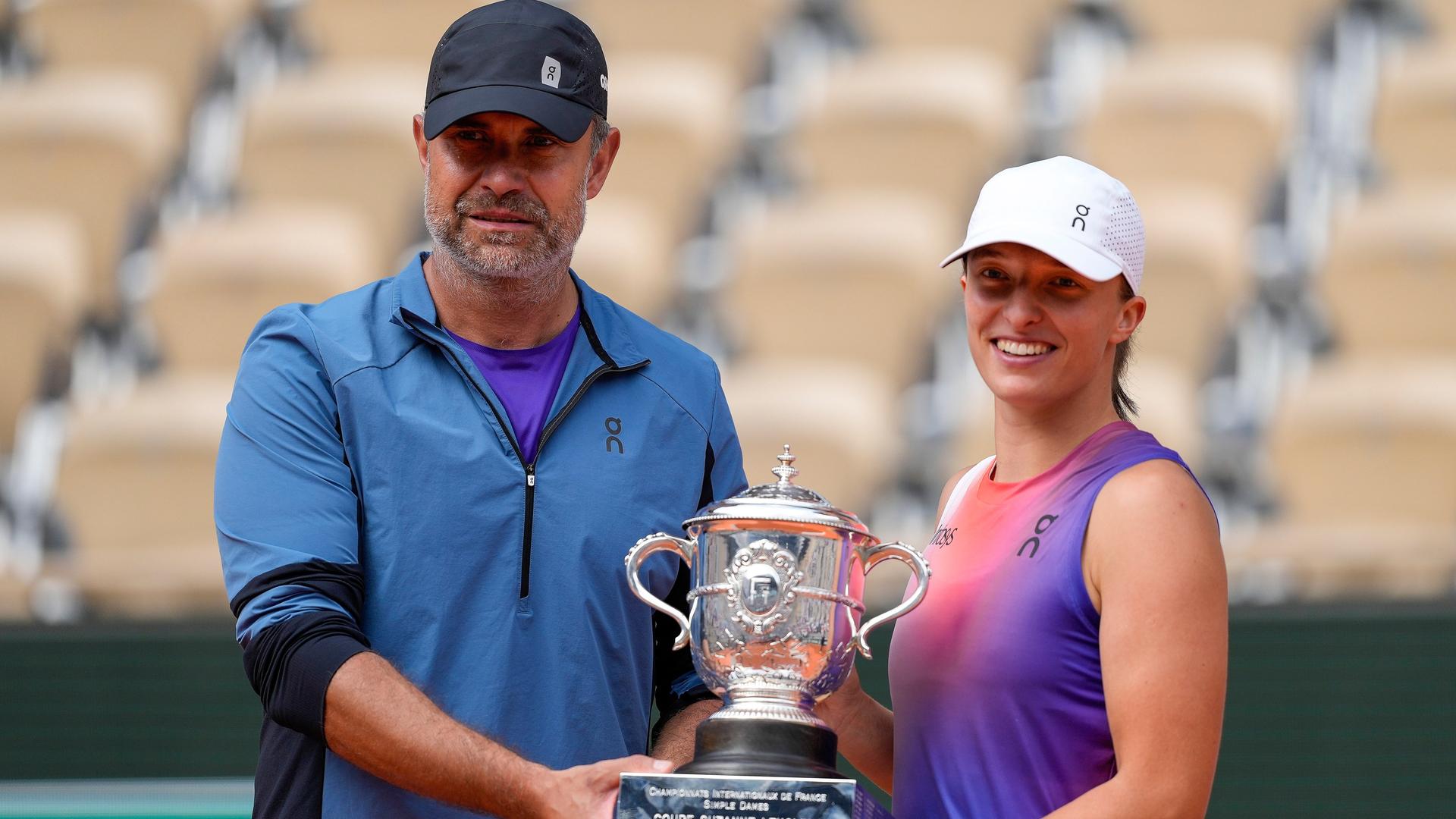 Die Tennis-Weltranglistenerste Iga Swiatek mit ihrem Trainer Tomasz Wiktorowski nach dem Gewinn der French Open. Beide halten den Siegerpokal fest und lächeln in die Kamera.